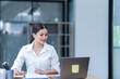 © Tj - Sharing good business news. Attractive young businesswoman talking on the mobile phone and smiling while sitting at her working place in office and looking at laptop PC.