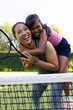 © wavebreak3 - Outdoors biracial mother and daughter smiling with tennis rackets on court