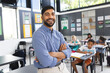 © Wavebreak Media - In school, Asian male teacher stands smiling with arms crossed in the classroom