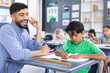 © Wavebreak Media - A young Asian male teacher smiles, guiding biracial boy in writing