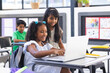 © Wavebreak Media - Two biracial girls, one in white dress, use a laptop in a classroom