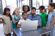 © Wavebreak Media - In school, young Asian male teacher and diverse students gather around a laptop in the classroom