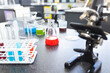 © Wavebreak Media - A microscope sits next to colorful liquid-filled beakers and test tubes on a lab bench in school