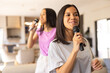 © Wavebreak Media - Biracial young sisters, singing with microphones at home, showcase long, dark hair