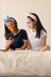 © Wavebreak Media - Two biracial young sisters at home, wearing headbands, looking at smartphone, in face masks