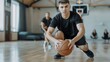 © Mikus - A man atop a hardwood floor, holding a basketball, addresses a seated audience on a basketball court The sphere rests before him