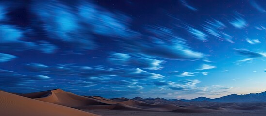 Wall Mural - nightly desert hills and dunes under a starry sky with clouds in blue hues, ideal for a photo with c