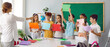 © Studio Romantic - Elementary school students showing blank paper sheets to teacher in classroom. Group of cute children standing around big classroom table, playing educational game together. School education concept