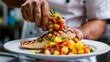 © Plaifah - A chef presenting a plate of grilled fish steaks with a colorful mango salsa, showcasing the vibrant flavors and textures of the seafood dish.