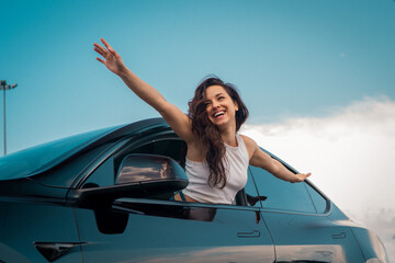 Positive brunette lady enjoying travel while sticking out the side view window and holding hands to the side. Travel adventure drive, happy summer vacation concept