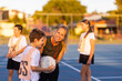 © Austockphoto - woman coaching children in netball team, leaning over child and looking at camera