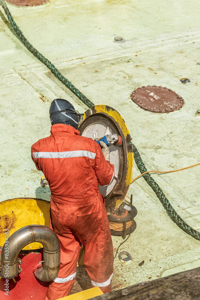 metal worker in orange overalls is working with a grinder on board a ship