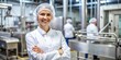 © guntapong - Sterile uniformed female food factory manager with arms crossed and hair net, smiling at the camera, success, food industry, factory, women, manager, hygiene, quality control, leadership