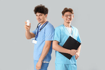 Wall Mural - Male medical interns with pill bottle and clipboard on light background