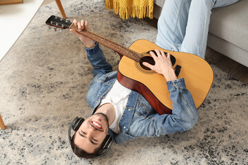 Canvas Print - Young bearded man in headphones playing guitar at home