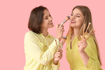 Wall Mural - Female friends with makeup brushes on pink background