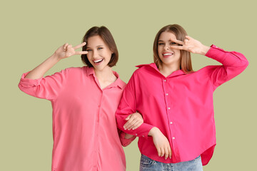 Wall Mural - Female friends showing victory gesture on green background