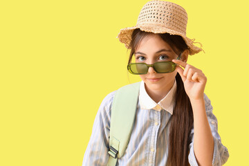 Wall Mural - Cute little tourist in sunglasses with backpack on yellow background, closeup