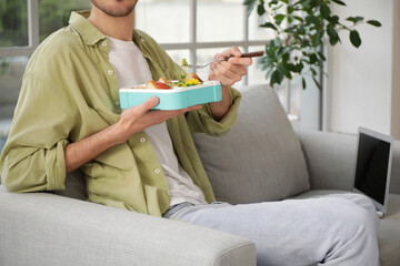 Sticker - Young man with lunchbox sitting on sofa at home, closeup