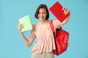 Wall Mural - Happy female student with backpack and notebooks on blue background