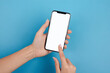 © Adam - Woman's hand holding mobile phone and finger touches blank screen screen with copy space, isolated on a blue background