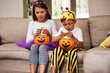 © peopleimages.com - Halloween, sweets and children on sofa with costume for holiday event, celebration and happiness with pumpkin. Couch, young girl and boy with orange vegetable for eating candy, smile and fairy outfit