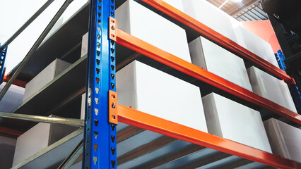 Fototapete - A stack of white boxes in warehouse on a blue and orange rack. The boxes are stacked on top of each other and are all the same size