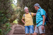 © luciano - Happy couple of senior males friends in a trekking day in the forest enjoying healthy lifestyle and nature, two elderly men holding backpack