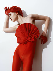 Beautiful redhaired woman in red bodysuit posing against white wall in minimalist fashion shoot