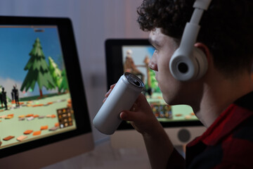 Wall Mural - Young man with energy drink playing video game at wooden desk indoors, closeup