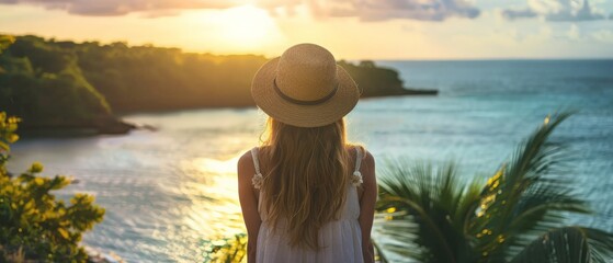 Canvas Print - A young woman, adorned with a hat, overlooks a calm sea in a lush tropical setting. The wide shot captures the serene vibe, bathed in the warm glow of golden hour light.