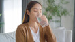 © Monster Ztudio - Happy young Asian woman drinking water while sitting on the sofa in the living room