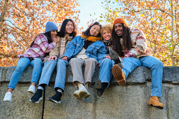 Multiethnic group of five friends hugging, having fun, laughing and looking at camera at street in autumn.