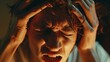 © Spot Decor - Close-up of young man grimacing in pain from intense migraine or headache, cradling his head.
