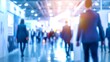 © OMD - Blurred image of business people walking in a modern exhibition hall, with bright lights and stands in the background.