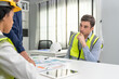 © Supachai - Construction team engineers in safety vests discussing project plans in office, with thoughtful male leader and charts on the table.