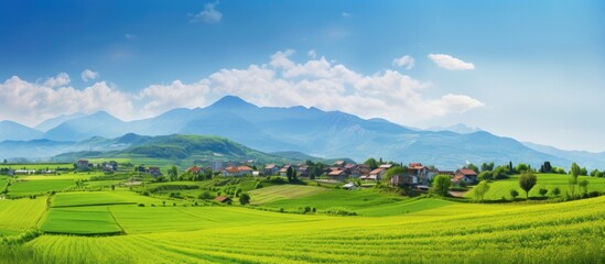 Wall Mural - Scenic landscape with a mountain backdrop, lush green fields, a clear blue sky, and a charming village in the background, perfect for a copy space image.