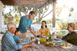 © peopleimages.com - Table, food and family outdoors for lunch, supper and eating meal in backyard together. Celebration, parents and children with dish for bonding, relax and talking for nutrition, health and wellness