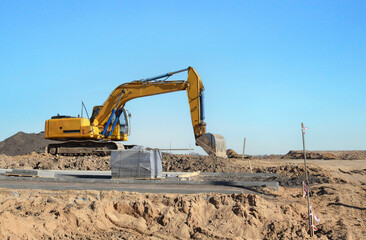 Wall Mural - Excavator on earthmoving at construction site. Backhoe digs sand on blue sky background. Construction machinery for excavation, loading, lifting and groundwork on job sites.