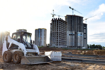 Poster - Skid-steer loader for loading and unloading works on city streets. Сompact construction equipment for work in limited conditions. Road repair at construction site. Tower cranes during construction