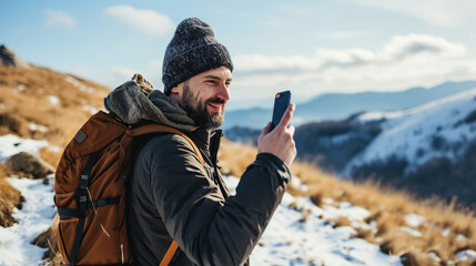 Wall Mural - A man with a backpack and a hat is smiling while taking a picture with his cell phone. Concept of adventure and enjoyment of the outdoors