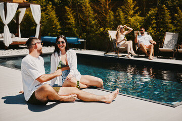 Wall Mural - Young group of people drinking beer and having fun by the pool