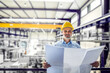 © Halfpoint - Portrait of project manager reading blueprint modern industrial factory. Manufacturing facility with robotics, robotic arms and automation. Storing products and materials in warehouse.