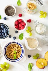 Wall Mural - Top view different ingredients for cooking a healthy breakfast setup with granola, assorted fresh fruits, chia seeds and yogurt on a white marble background