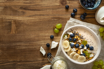 Wall Mural - Healthy breakfast bowl topped with fresh fruits, yogurt, granola, chia seeds and coconut on a rustic wooden table with copy sapce. Weight loss, healthy and nutritious food, op view