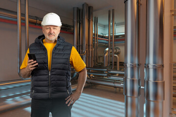 Poster - Man engineer standing in basement. Worker in industrial premises. Engineer with phone calls contractor. Builder inside boiler room. Engineer in basement with pipes. Man inspects production equipment