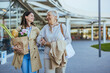 © Dragana Gordic - A smiling young woman helps her senior mother carry fresh groceries outside a store, both dressed in light casual wear, exemplifying family care and support.