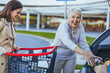 © Dragana Gordic - A cheerful Caucasian woman helps her elderly mother by placing shopping bags into the trunk of a car in a parking lot.