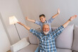 © Dragana Gordic - Laughing grandfather with his grandson as they play together indoors in the living room with the cute young boy hugging him from behind. Carefree child and a happy grandpa