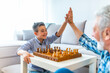© Dragana Gordic - Happy little kid playing chess with senior man at home. Family relationship with grandfather and grandson. Grandpa and male grandchild playing board game